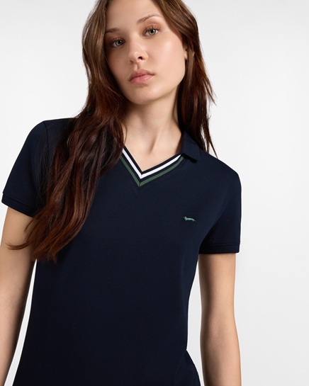 A model wears a short-sleeved navy blue Harmont & Blaine women's polo shirt with a V-neck trimmed with white and green stripes and the embroidered dachshund logo on the chest, in an image focused on the women's polo category.