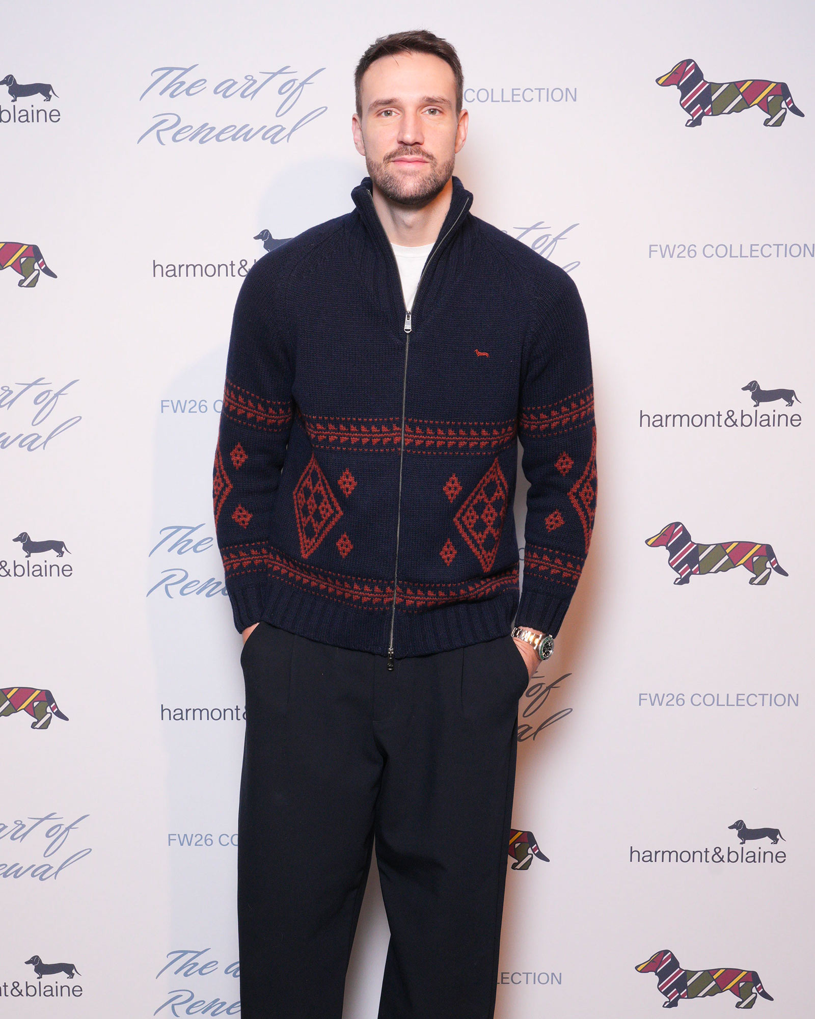 Homme portant pull marine &agrave; motifs g&eacute;om&eacute;triques rouges et pantalon sombre