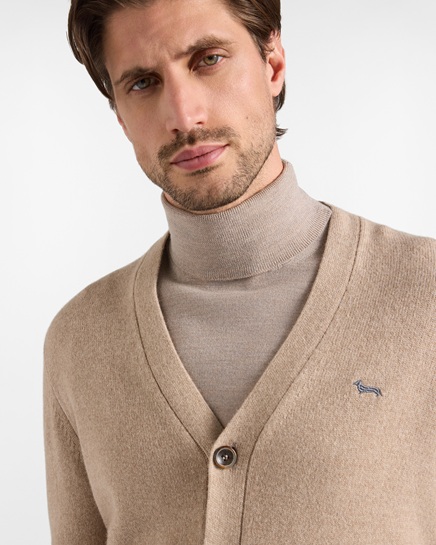 A model wears a beige V-neck cardigan with a front button closure over a matching Harmont & Blaine turtleneck sweater, enriched with the characteristic embroidered dachshund logo on the chest, in an image focused on the men's knitwear category.