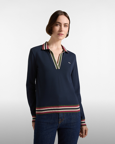 Una donna con capelli corti castani indossa una polo a maniche lunghe blu scuro da donna con profonda scollatura a V, dettagli a righe multicolore su colletto, polsini e bordo inferiore, abbinata a jeans scuri.