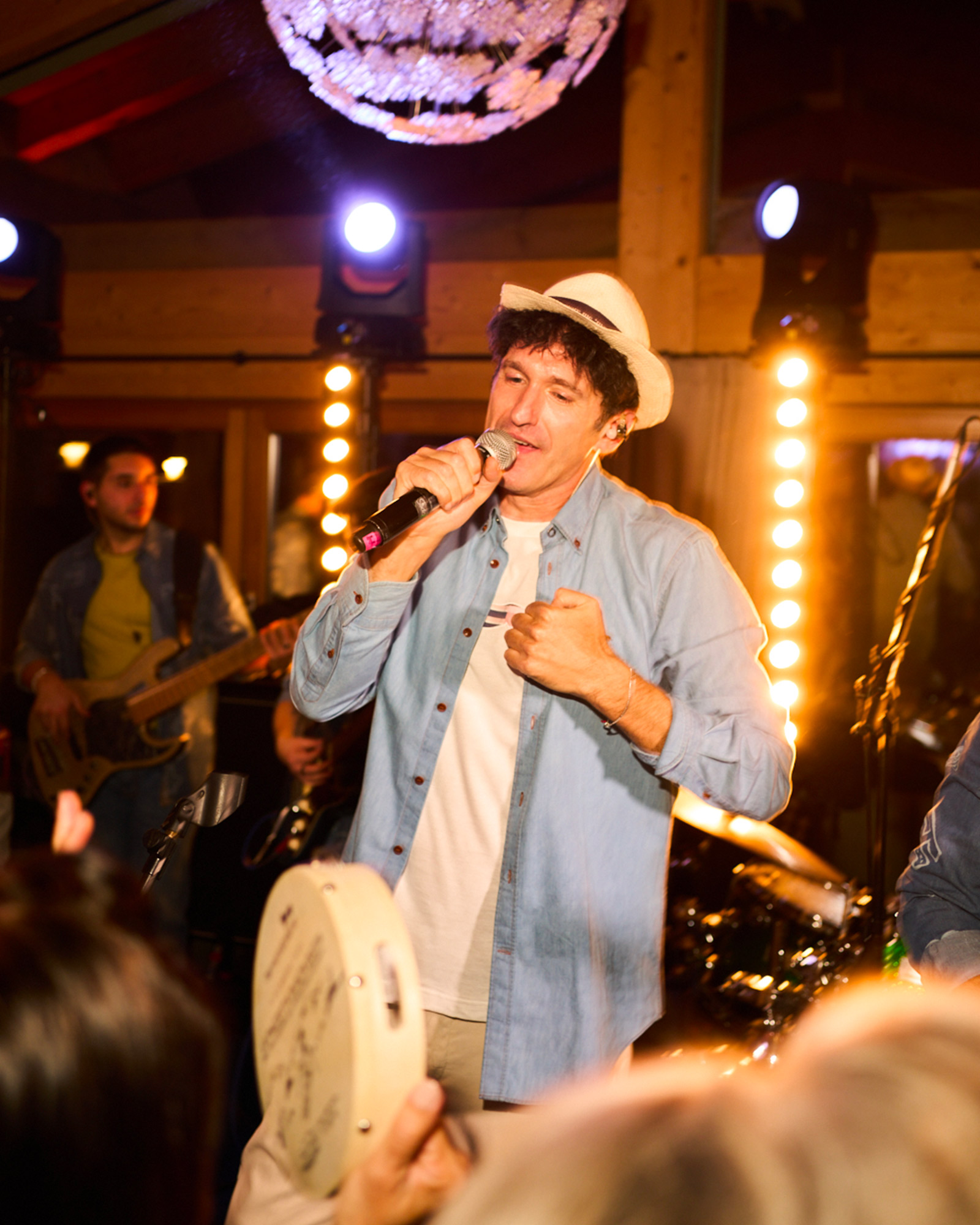 Singer wearing a denim shirt and light hat performing on stage.